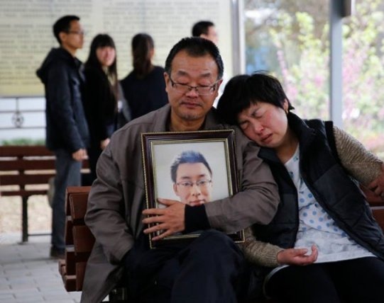 Wei Zexi’s parents, holding his portrait, wait outside the funeral home in Xianyang on 13 April 2016